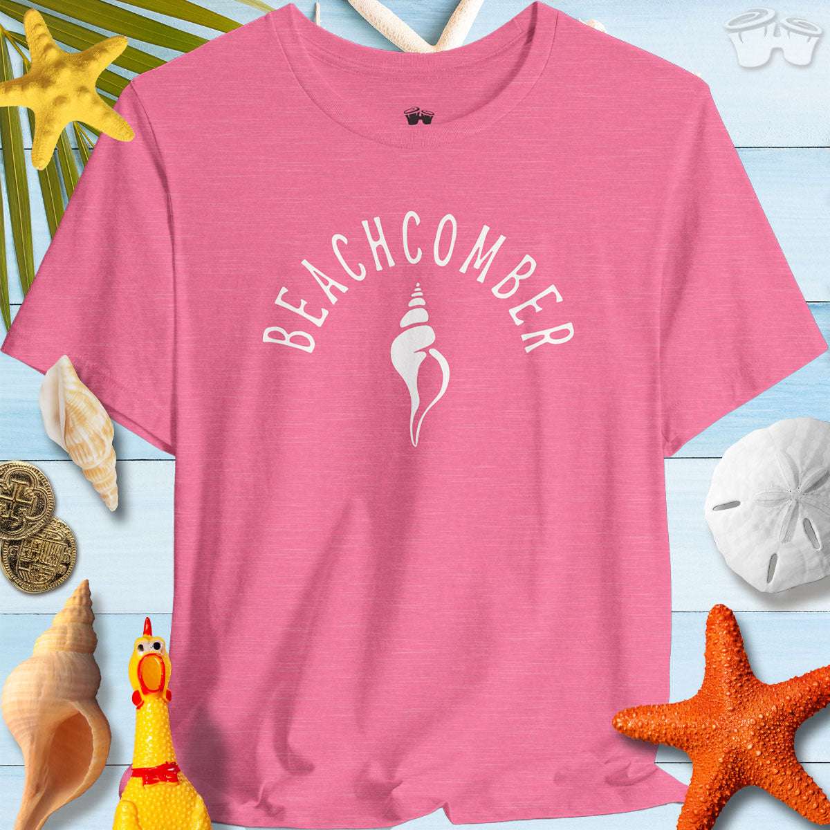 Pink Beachcomber shelling t-shirt surrounded by beach shells and starfish, perfect for summer adventures.