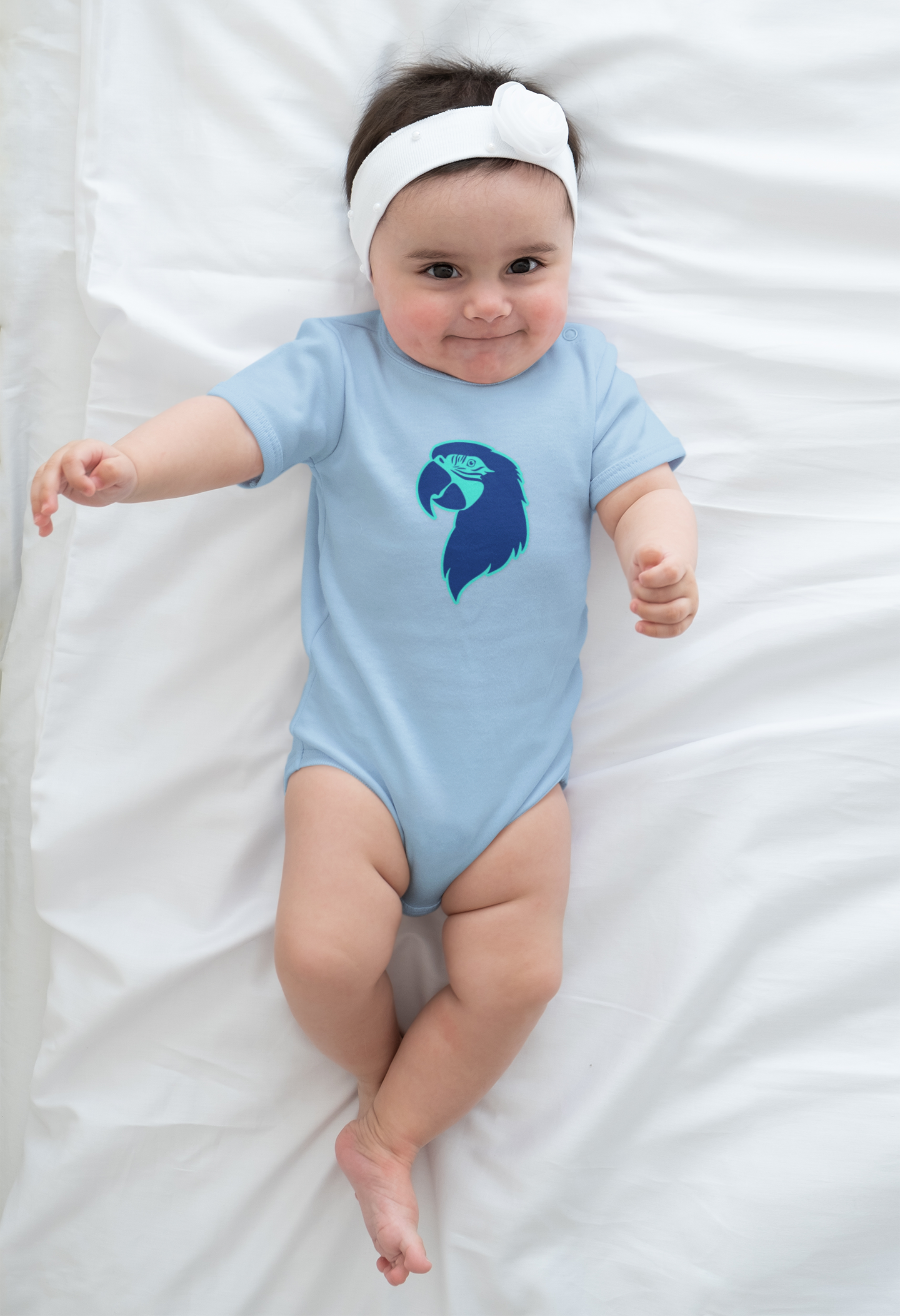 Baby wearing a light blue onesie with a blue parrot head design on a white blanket