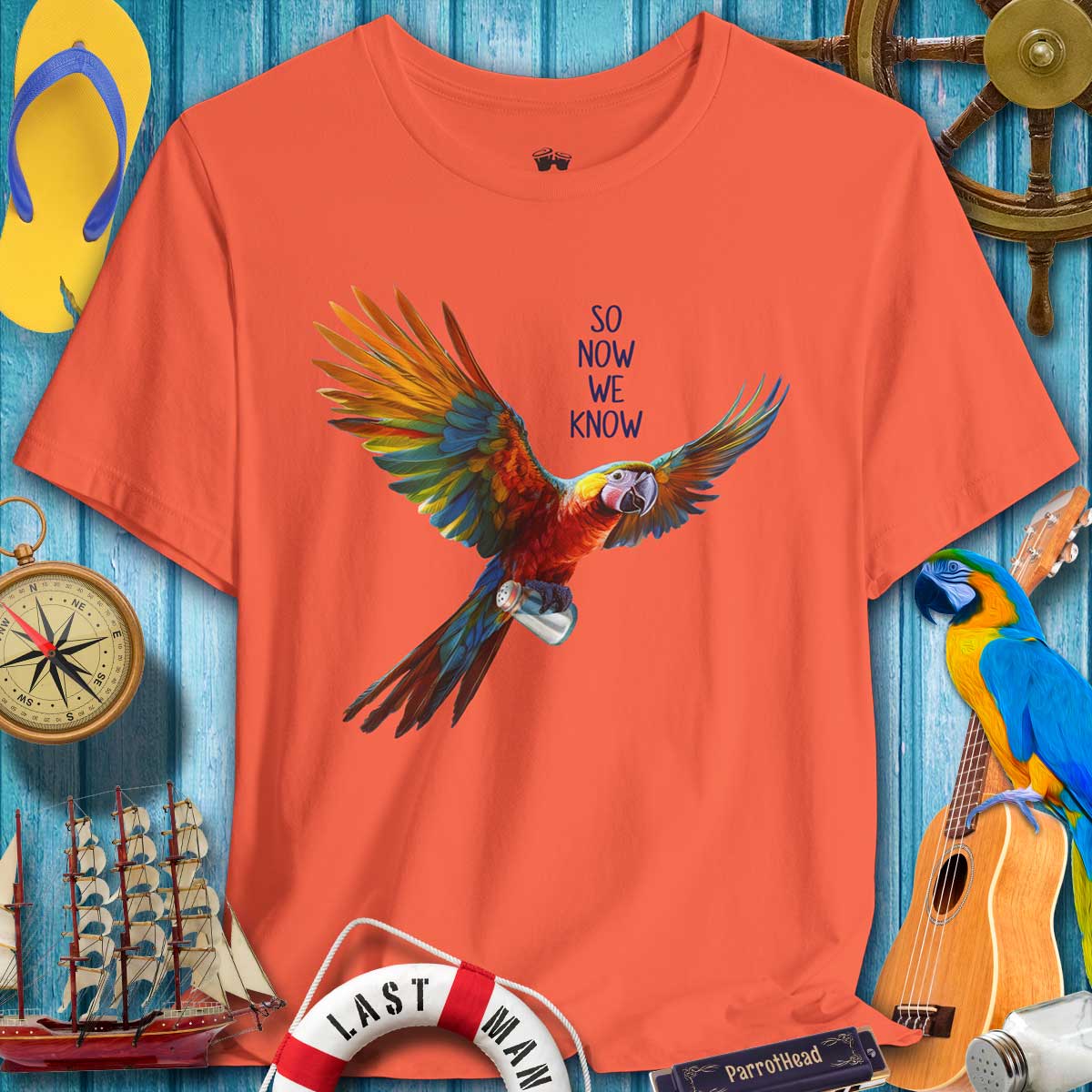 Orange t-shirt with a parrot graphic and text on a blue wooden background withautical items.