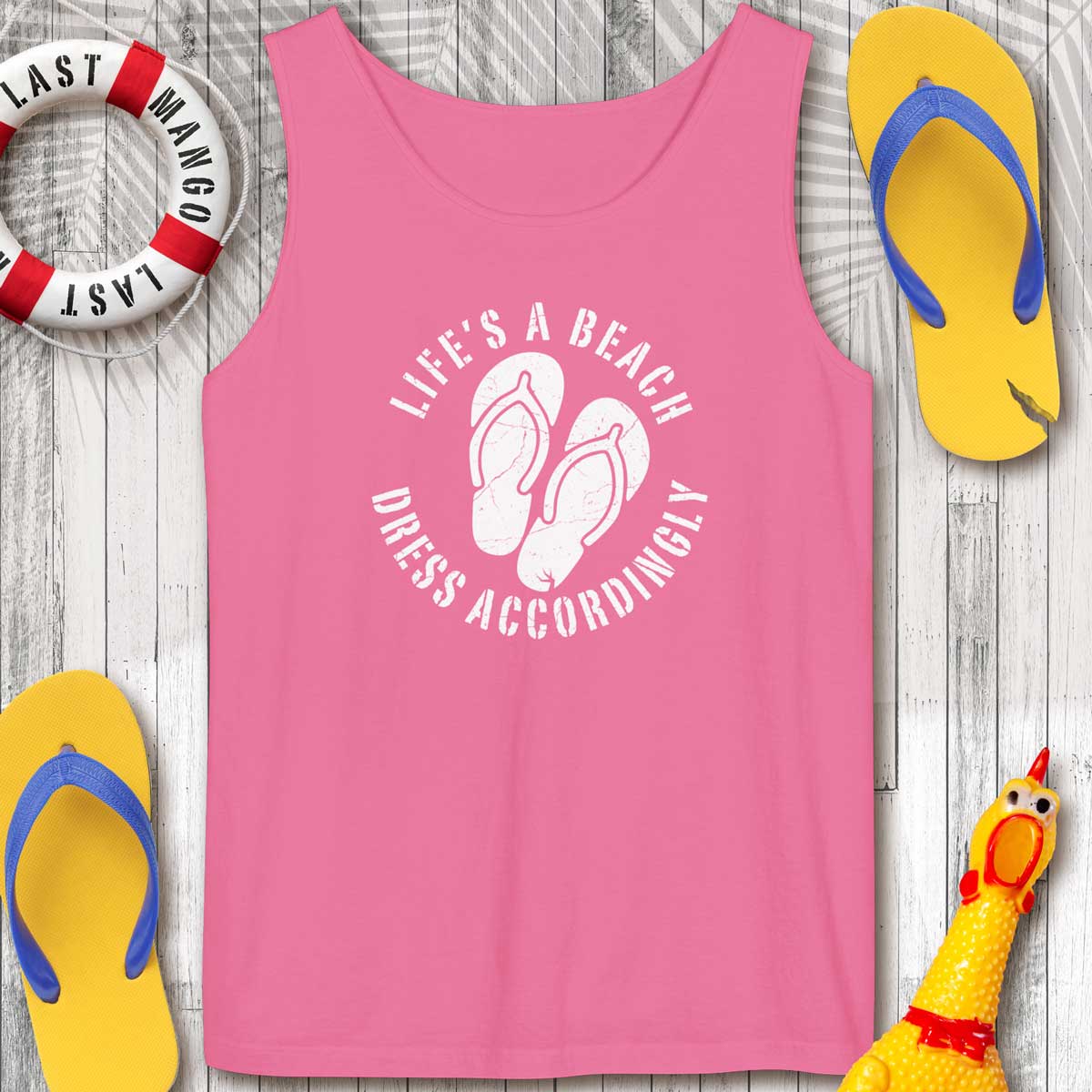 Pink tank top with 'Life's a Beach Dress Accordingly' text and flip-flops on a wooden surface.