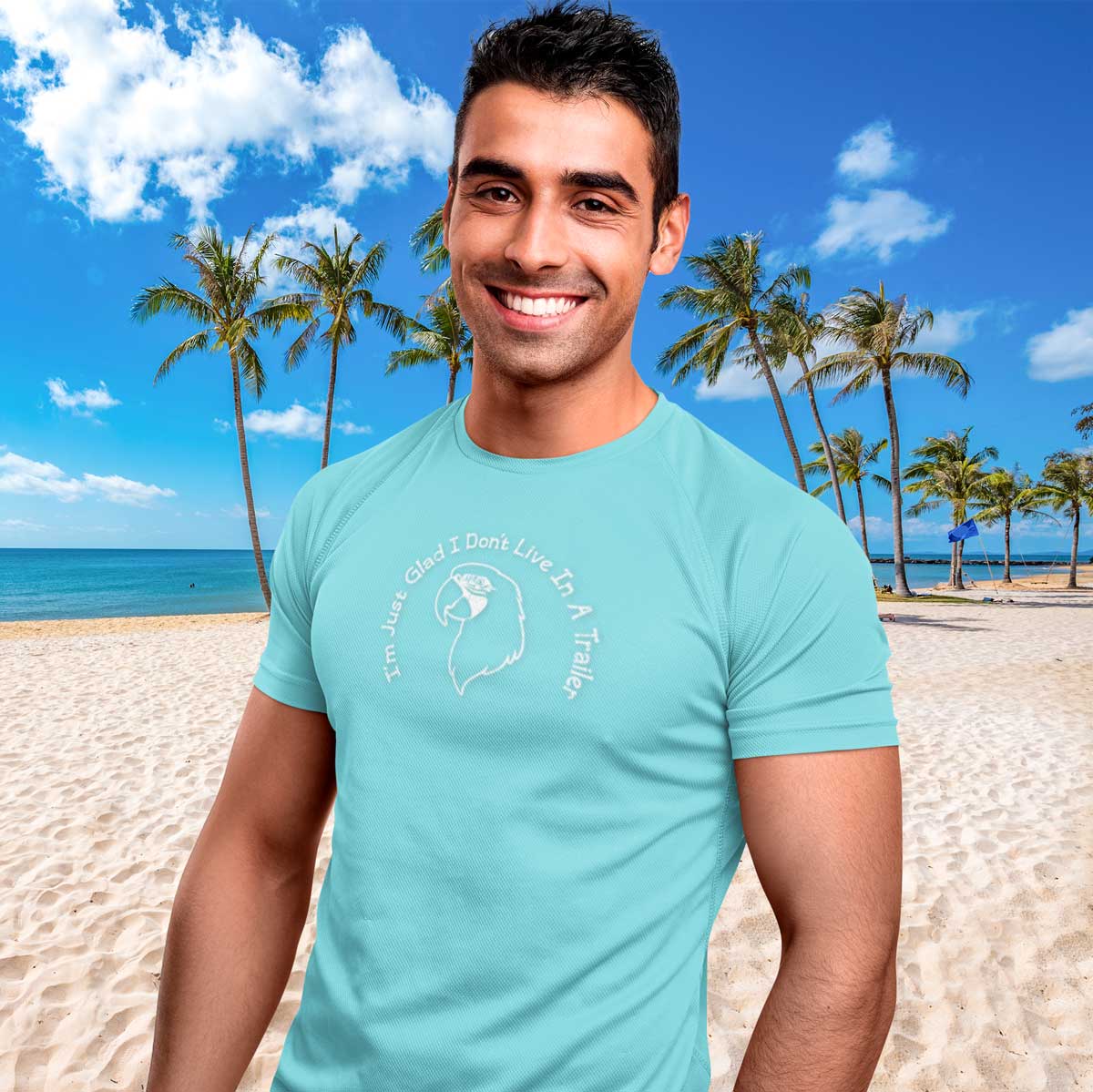 Man wearing a light blue t-shirt with a graphic design on a beach with palm trees and blue sky.