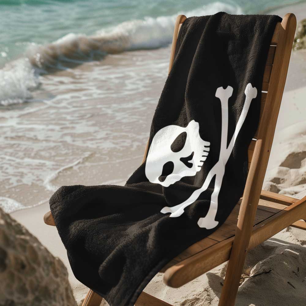 Jolly Roger Pirate Flag Beach Towel draped over a beach chair in the sand