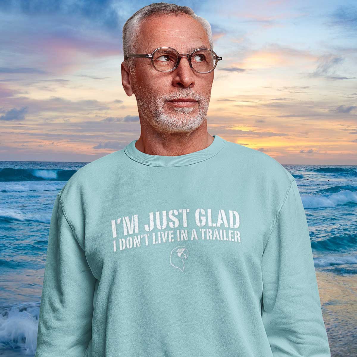 Man wearing a light blue sweatshirt with text standing against a scenic ocean backdrop