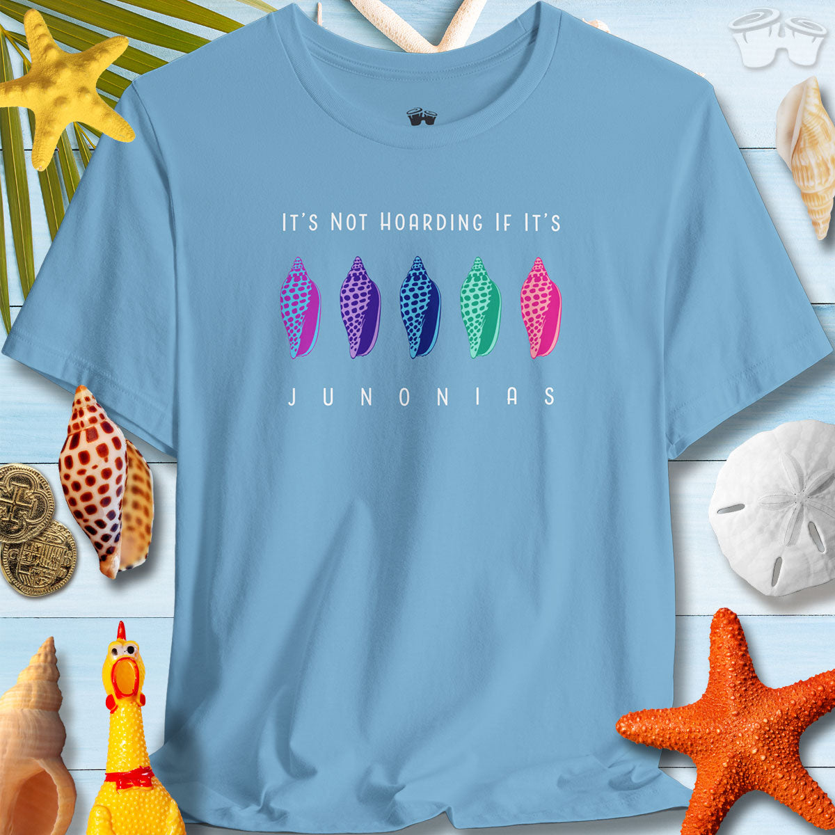 Colorful Junonia T-shirt on a beach backdrop with seashells, ideal for summer and beach lovers.