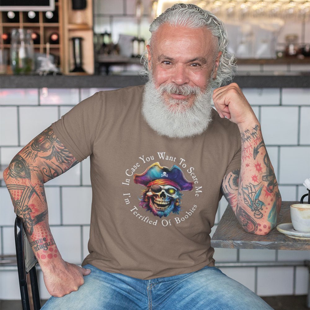 Man with tattoos wearing a brown t-shirt with a colorful graphic and text, sitting in a casual setting.