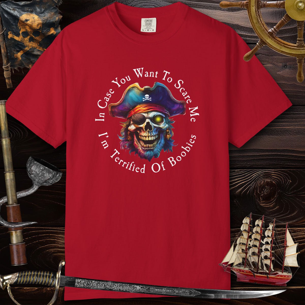 Red t-shirt with a pirate-themed graphic and text on a wooden background with ship and sword.