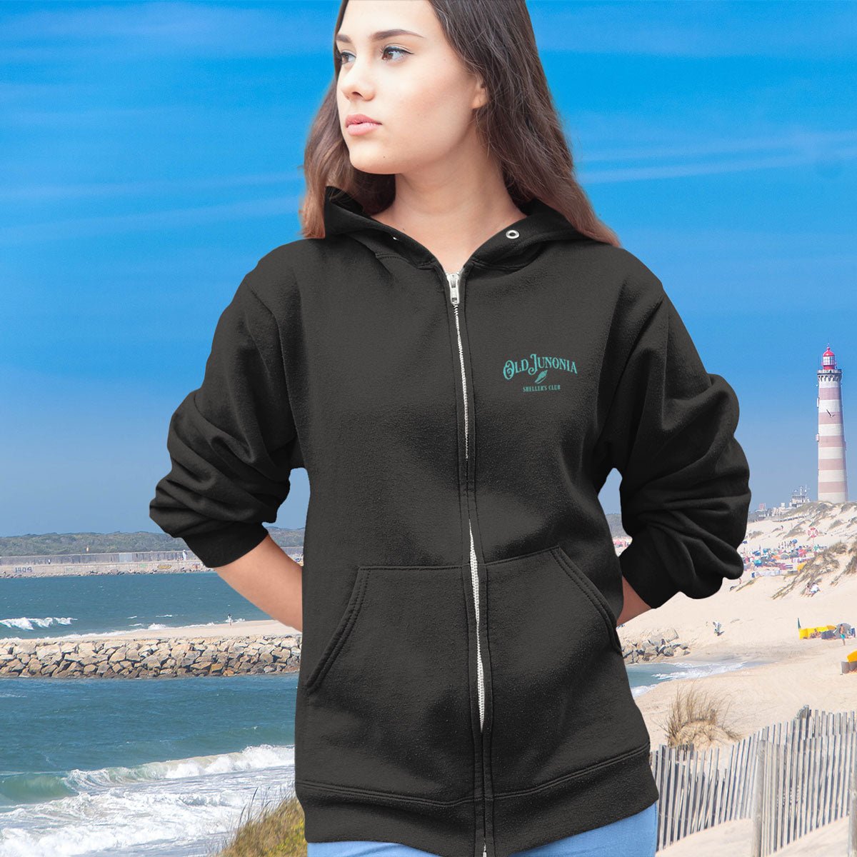 Person wearing a black hoodie with a logo on a beach