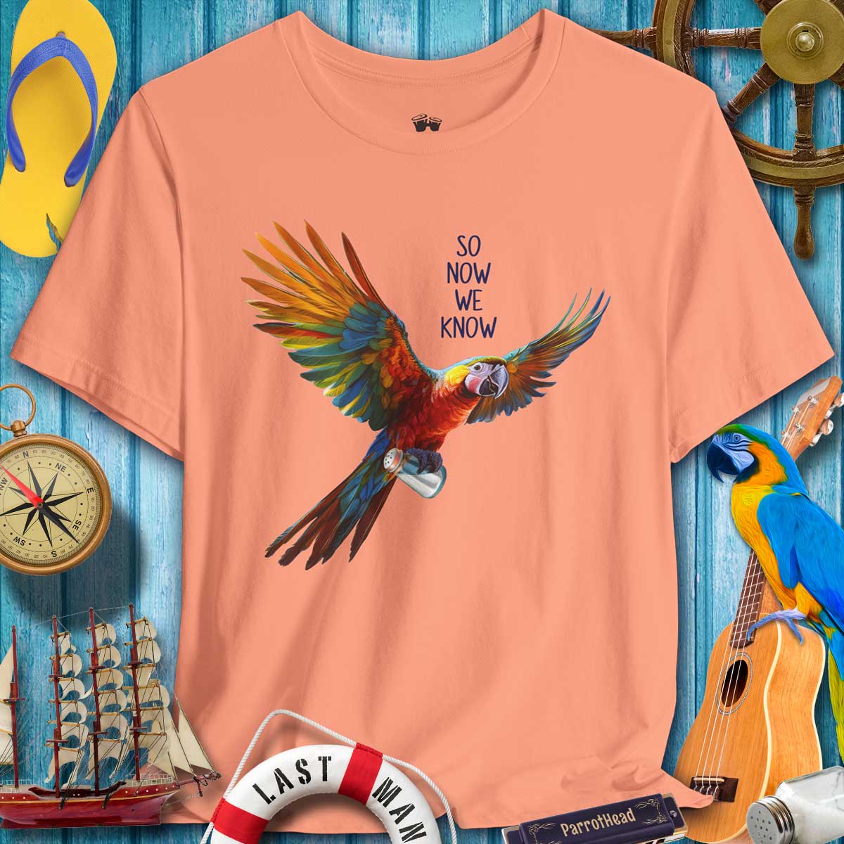 Peach t-shirt with a colorful parrot graphic and text on a blue wooden background with nautical items.