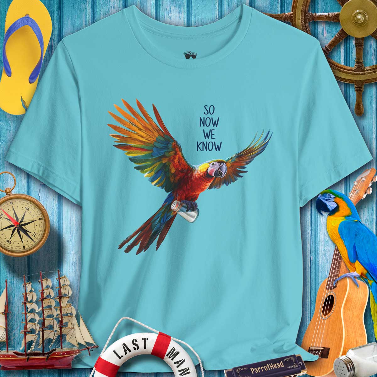 Blue t-shirt with a colorful parrot graphic and text, surrounded by nautical-themed items on a wooden background.