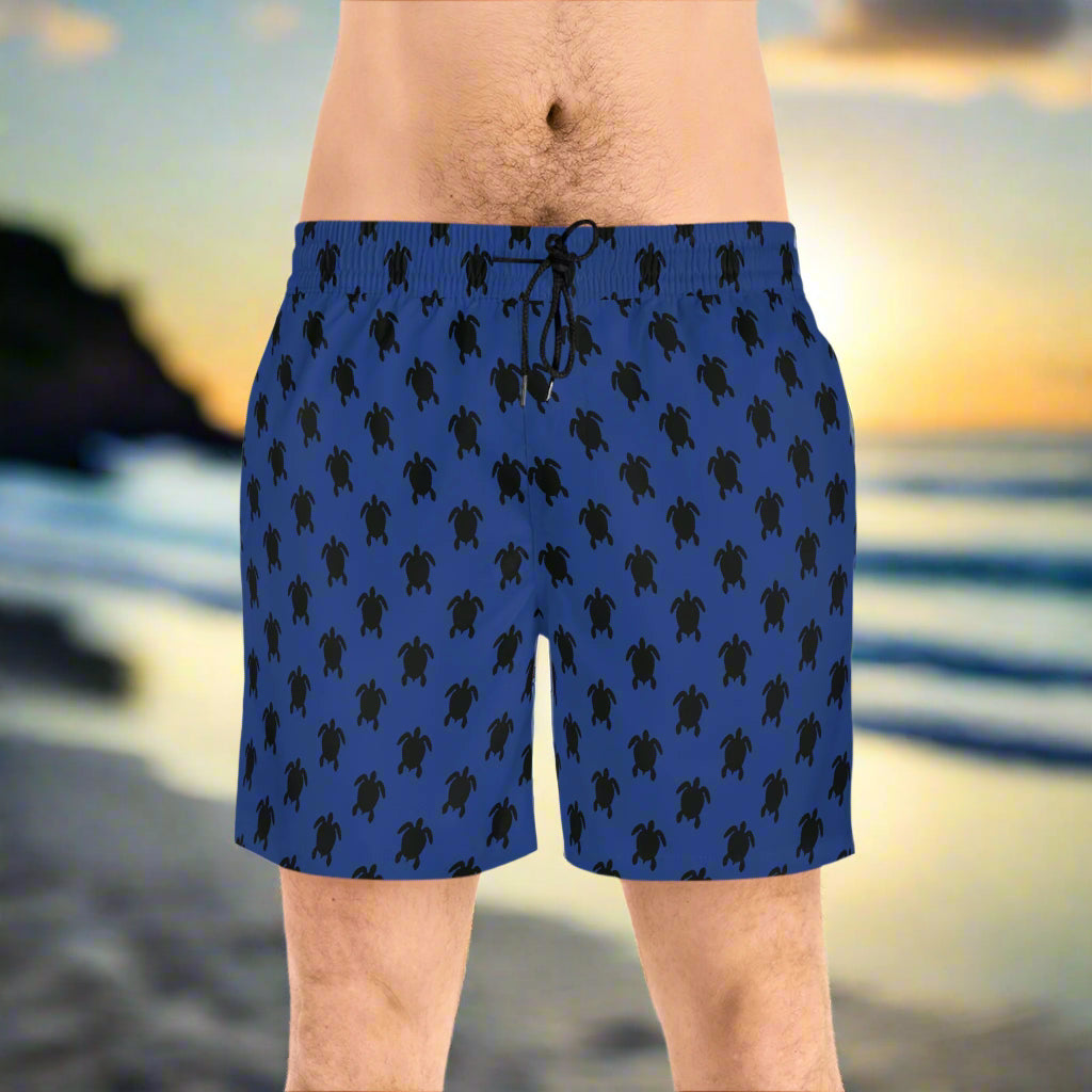 Guy wearing dark blue sea turtle board shorts with black tie string standing on the beach
