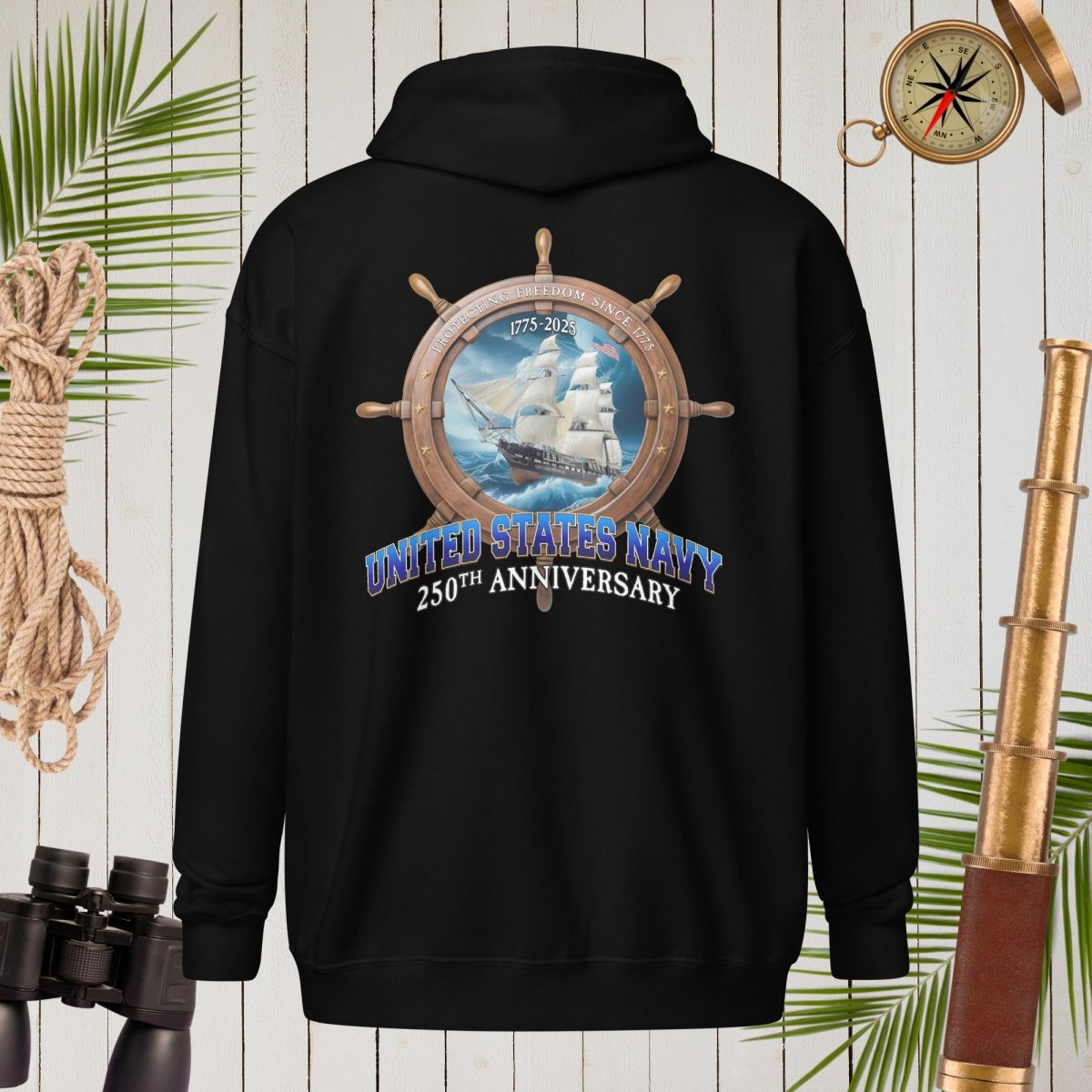 Black US Navy Hoodie with United States Navy 250th Anniversary design on a wooden background with nautical items.
