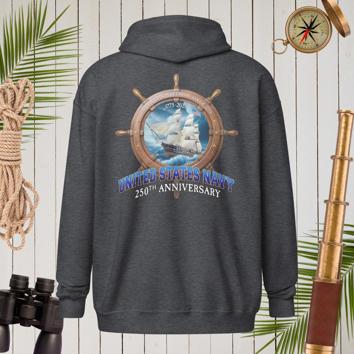 Dark gray hoodie with United States Navy 250th Anniversary design on a wooden background with nautical items.