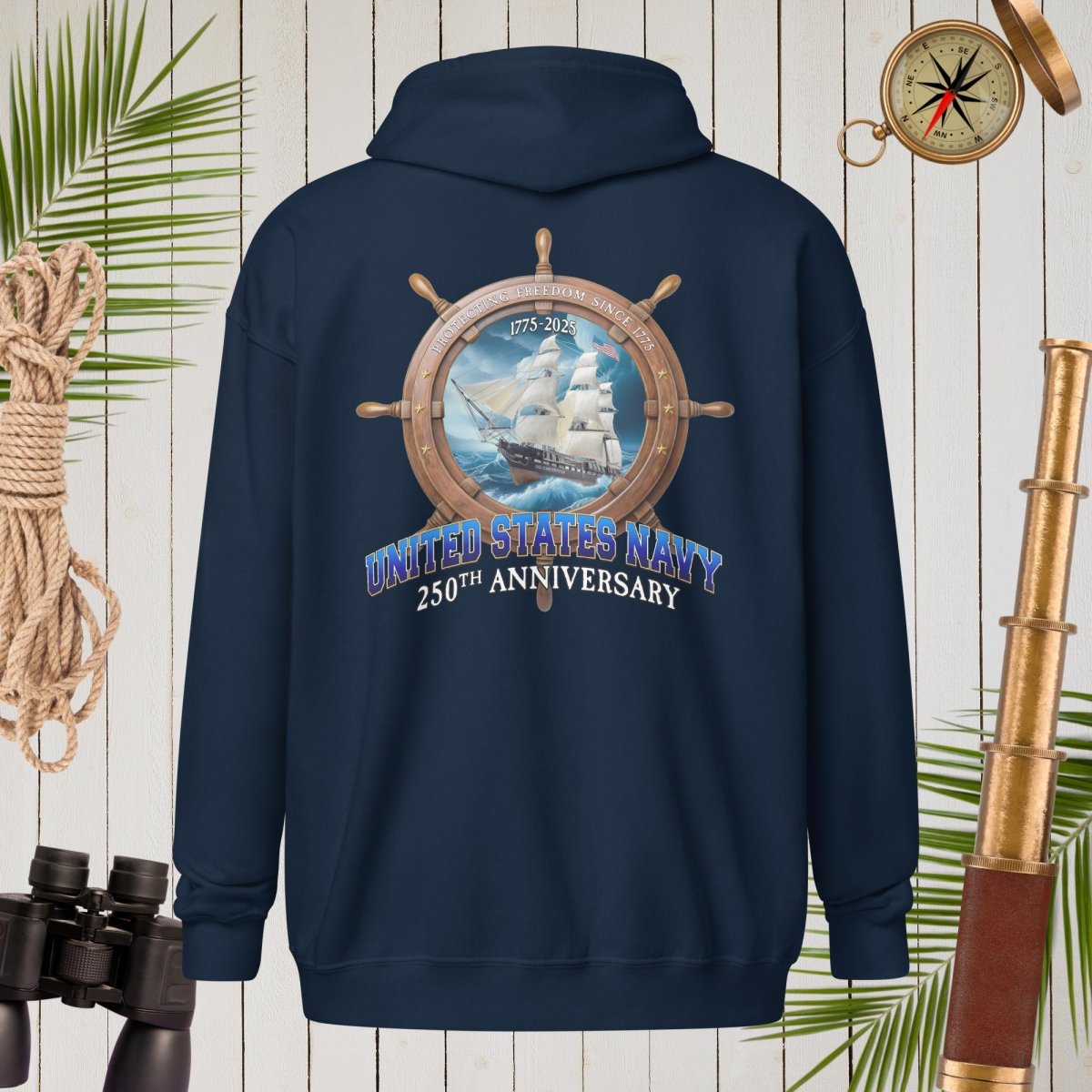 Navy blue hoodie with United States Navy 250th Anniversary design on a wooden background with nautical items.