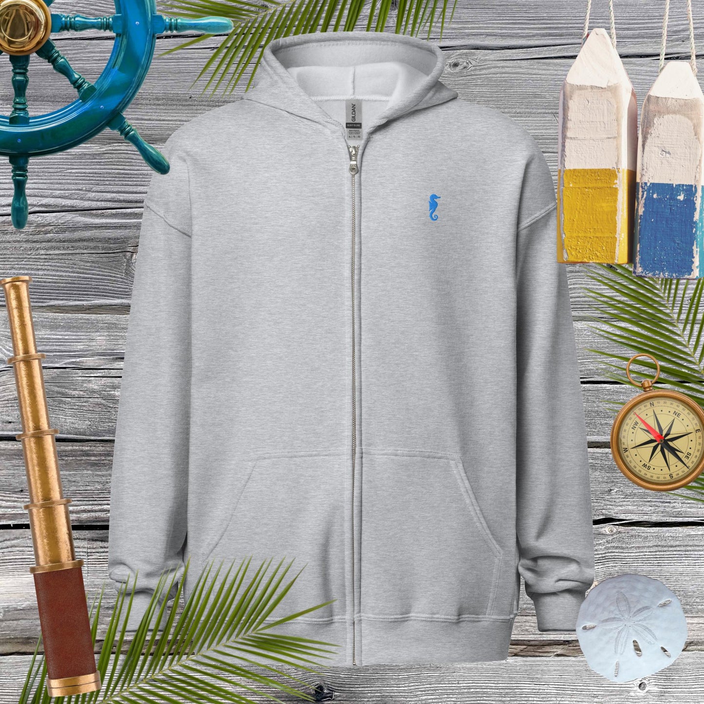 Unisex heavy blend zip hoodie with seahorse embroidery, set against nautical decor and palm leaves for a cozy vibe.