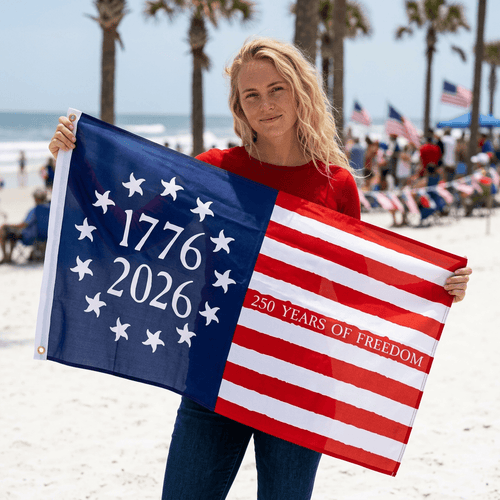 Person holding a flag with 1776–2026 250 Years of Freedom' on a beach.
