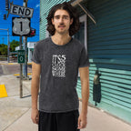 Person wearing a t-shirt with 'It's 5 o'clock somewhere' text on a street corner.