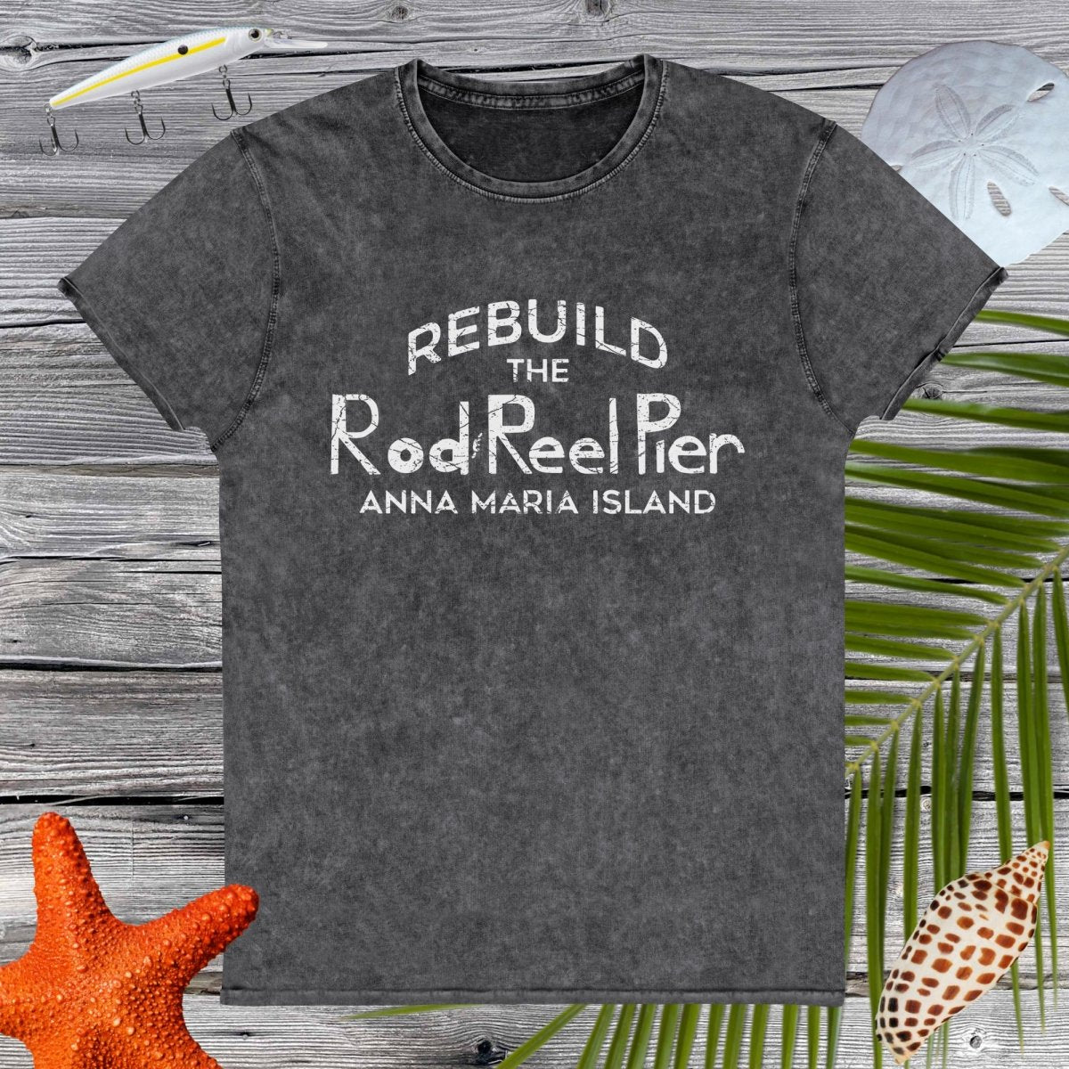 Dark Gray t-shirt with 'Rebuild the Rod Reel Pier Anna Maria Island' text on a wooden surface with beach elements.