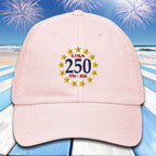 Pink cap with 'USA 250' design on a beach with fireworks background