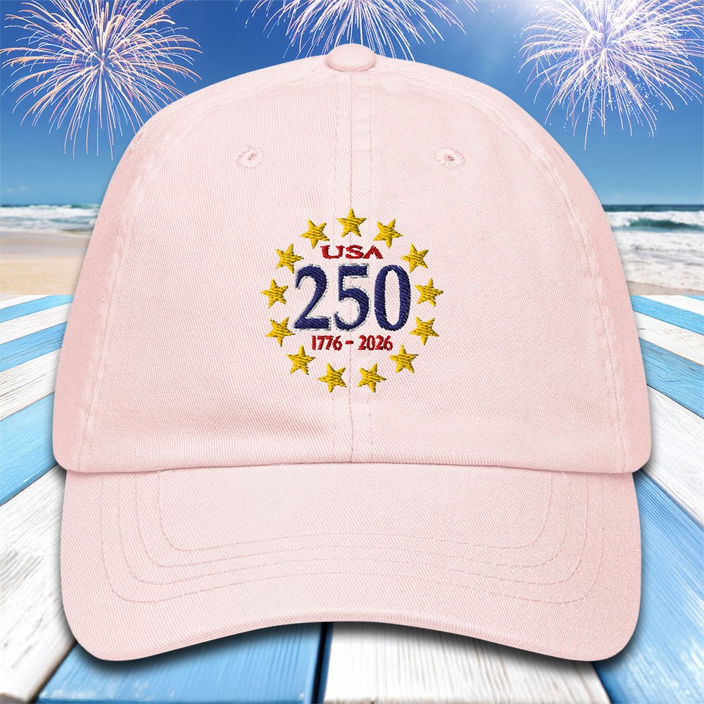 Pink cap with 'USA 250' design on a beach with fireworks background