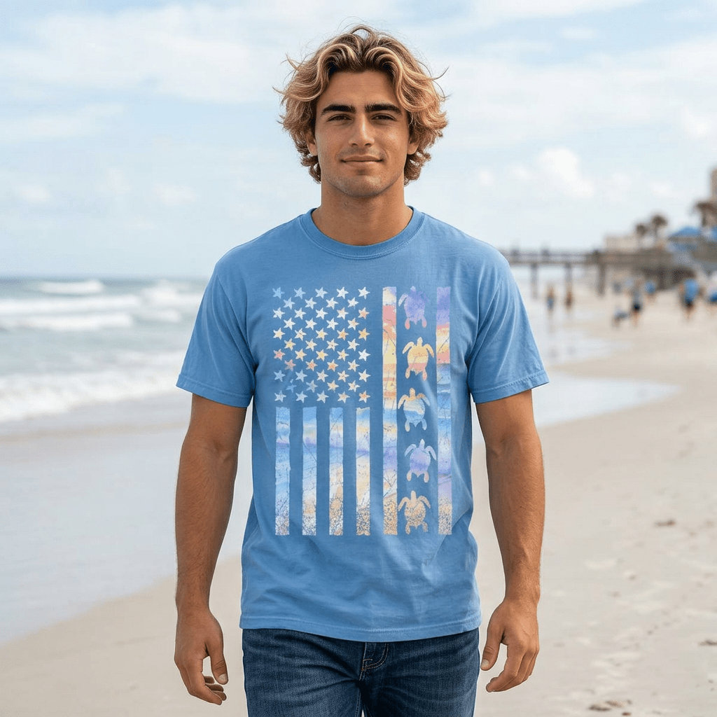 Man wearing a blue t-shirt with a colorful flag design on a beach
