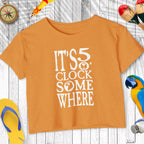 Orange t-shirt with 'It's 5 o'clock somewhere' text on a wooden surface with accessories.
