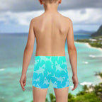 Boy wearing blue swim shorts with shark pattern looking out over Kailua Bay