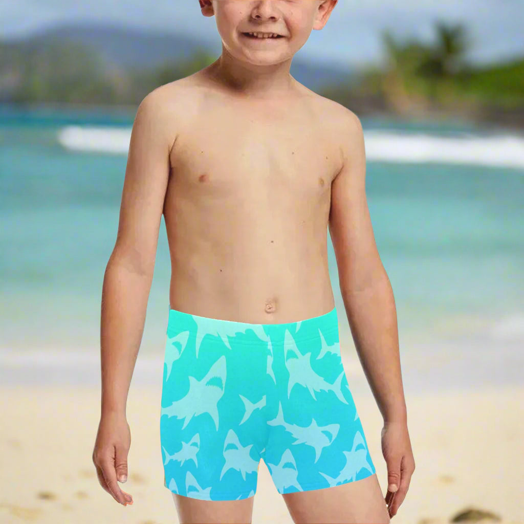 Boy wearing blue swim trunks with shark pattern hanging loose on Kailua Beach