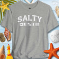 Salty Coastal Vibes Bella Canvas T-Shirt with nautical flags on a beach themed background.