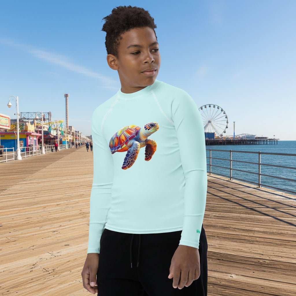 Teen dude wearing a light blue long-sleeve rashguard with a colorful turtle design on a white background