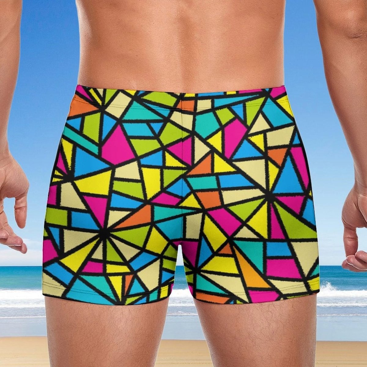 Backside of Colorful geometric patterned swim shorts for men with a beach background