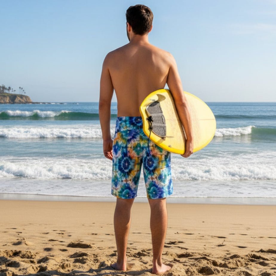 dude wearing tie dye board shorts holding a surfboard looking out at the ocean from La Jolla Beach