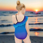 Girl wearing a blue and purple swimsuit with ruffled details on a beach at sunset