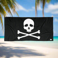 Jolly Roger Pirate Flag Beach Towel with skull and crossbones design hanging on a line in a tropical beach paradise