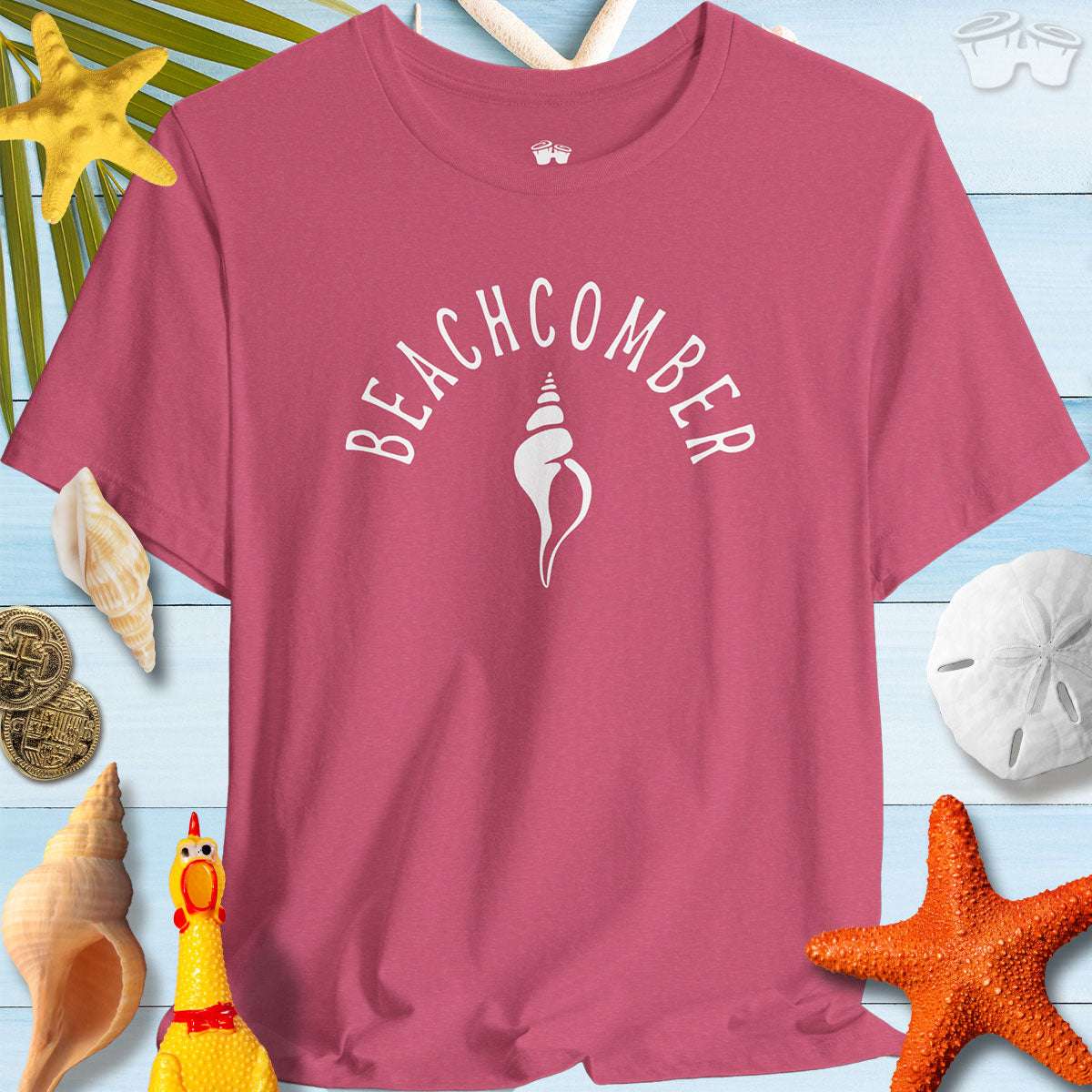 Beachcomber shelling T-shirt in pink, perfect for beach adventures, surrounded by seashells and beach decor.