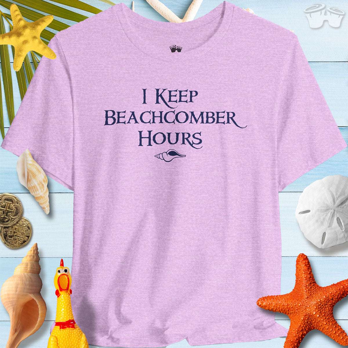 Beachy Bella shelling t-shirt in lavender with 'I Keep Beachcomber Hours' text, surrounded by beach items.