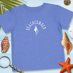 Blue t-shirt with 'BEACHCOMBER' design on a wooden surface with shells and a magnifying glass.