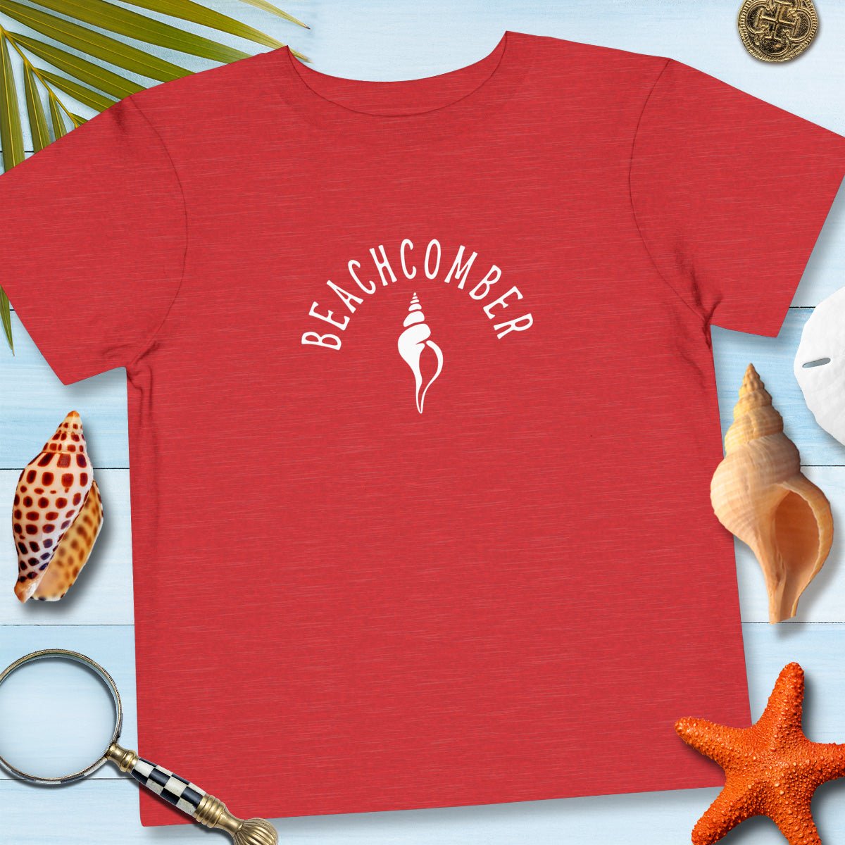 Red t-shirt with 'Beachcomber' design on a blue surface with beach-themed items.