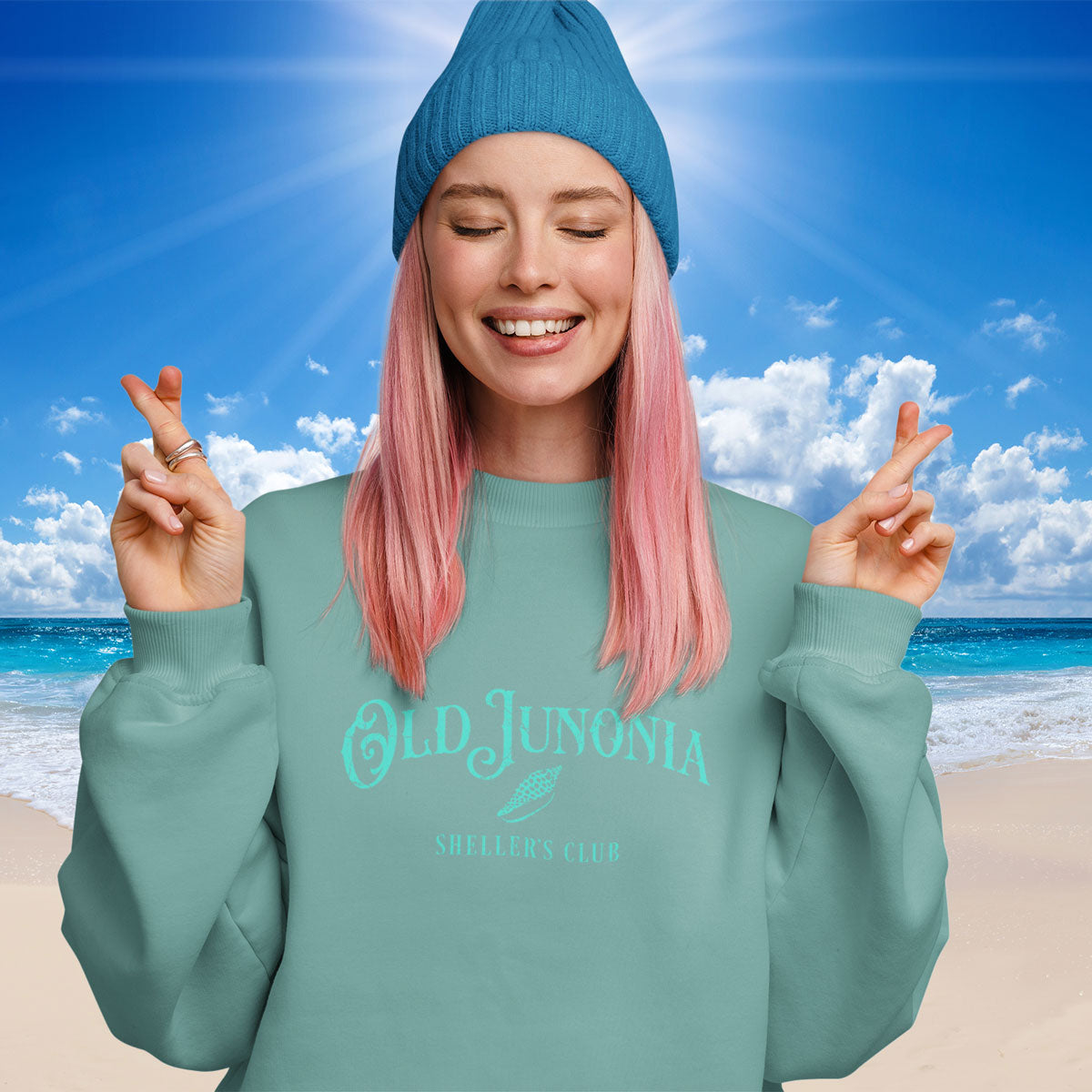Person wearing a teal sweatshirt with 'Old Junonia' text on a beach