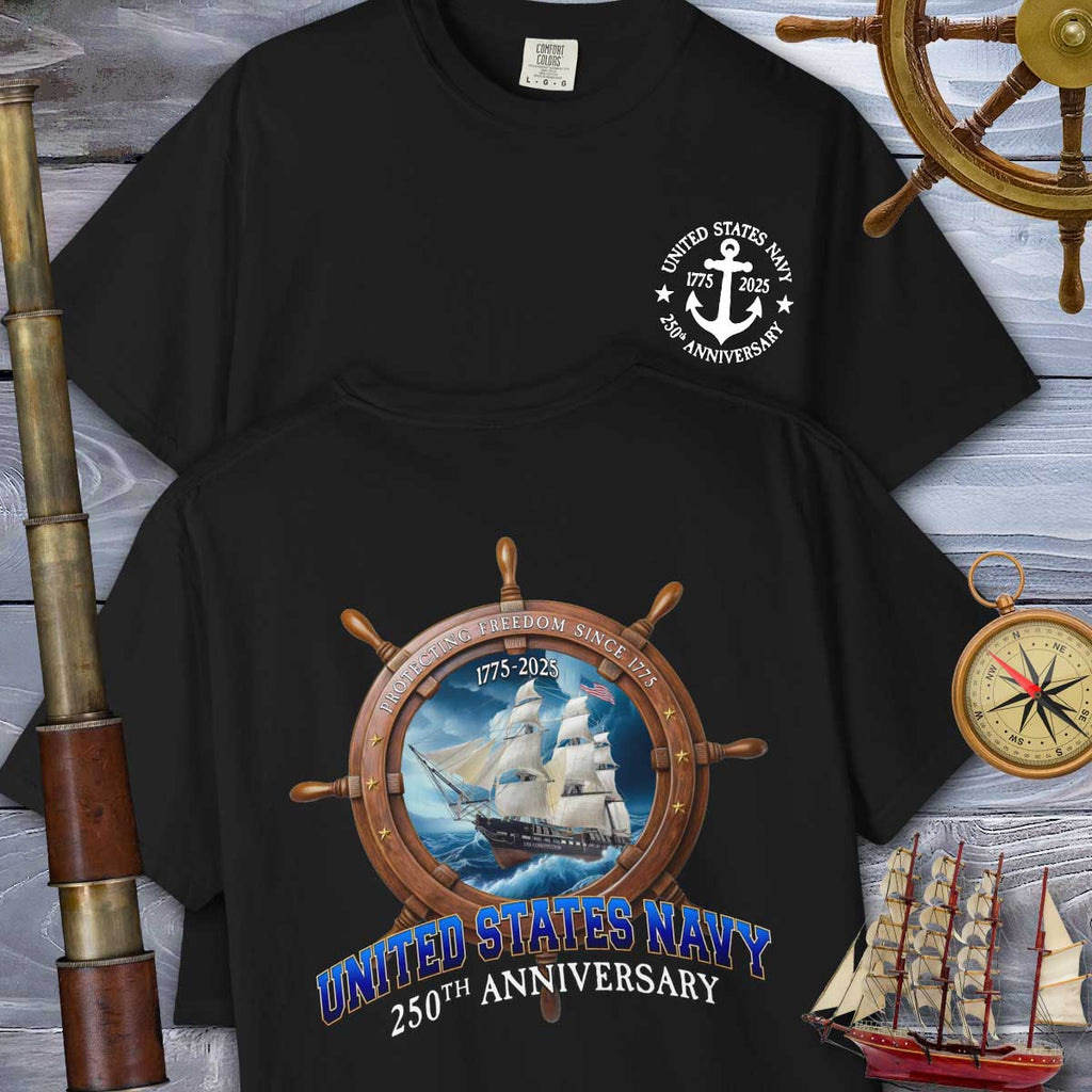 Black t-shirt with United States Navy 250th Anniversary design on a wooden background with ship and compass elements.