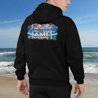 Person wearing a black hoodie with 'AMI Strong' design on a beach