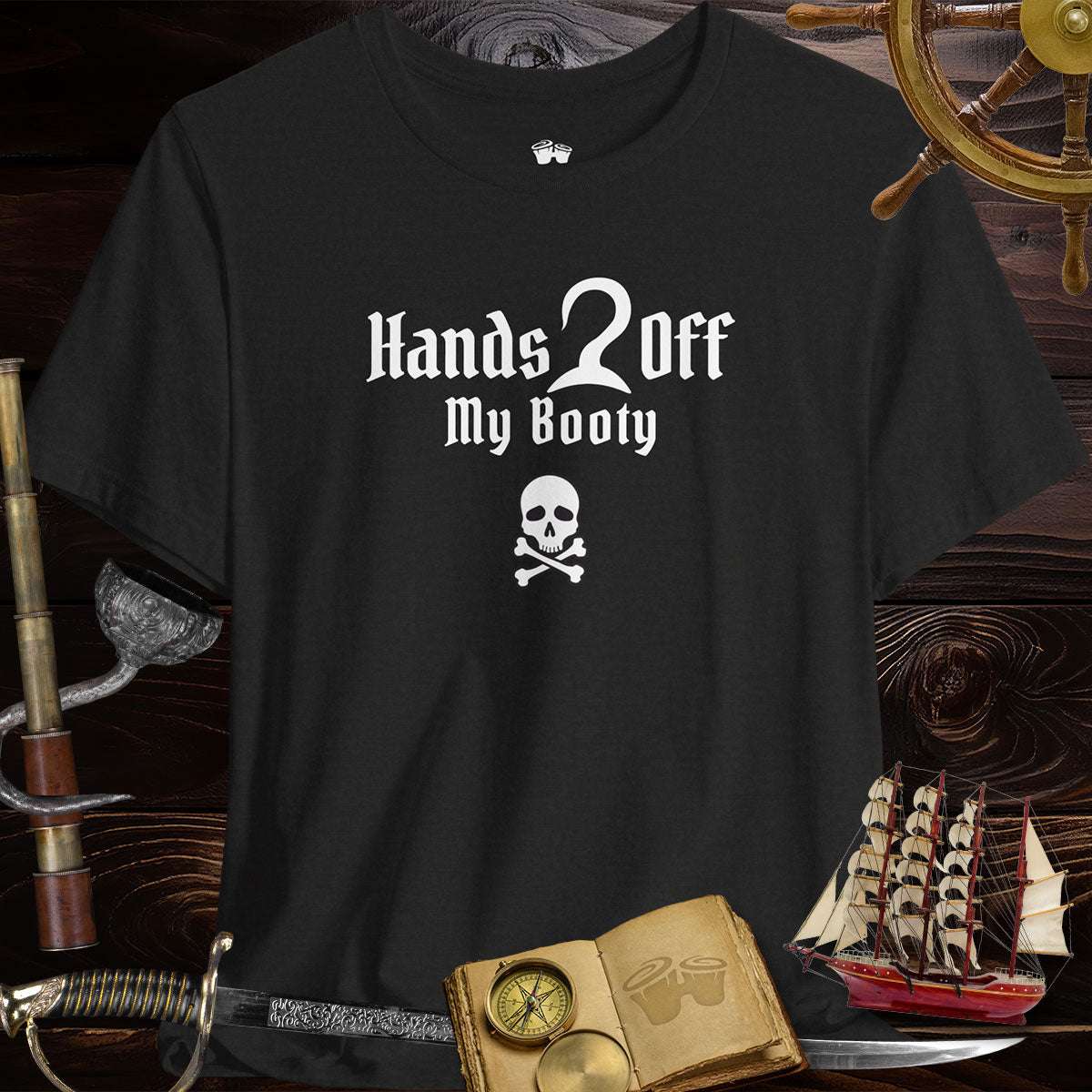 A Heather Black T-Shirt standing on it's own in front of a dark wood ships hull. Surrounded by a Helm, a spyglass with a hook, a ship's log, a sword, and model ship.