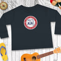 Black long-sleeve shirt with a logo on a wooden surface with a guitar, flip-flops, and compass.