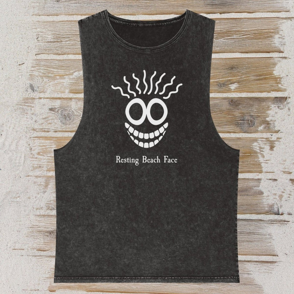 A dark washed sleeveless tank top laid flat on a rustic wood plank background. The shirt features a white graphic of a smiling face with wavy hair and the text 'Resting Beach Face' printed below.
