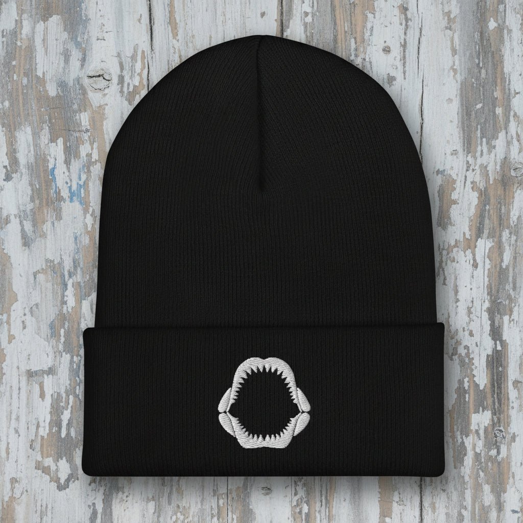 Black beanie with a white shark jaw embroidery on a rustic wood background