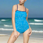 Model wearing blue dolphin bathing suit with navy staps standing on the beach