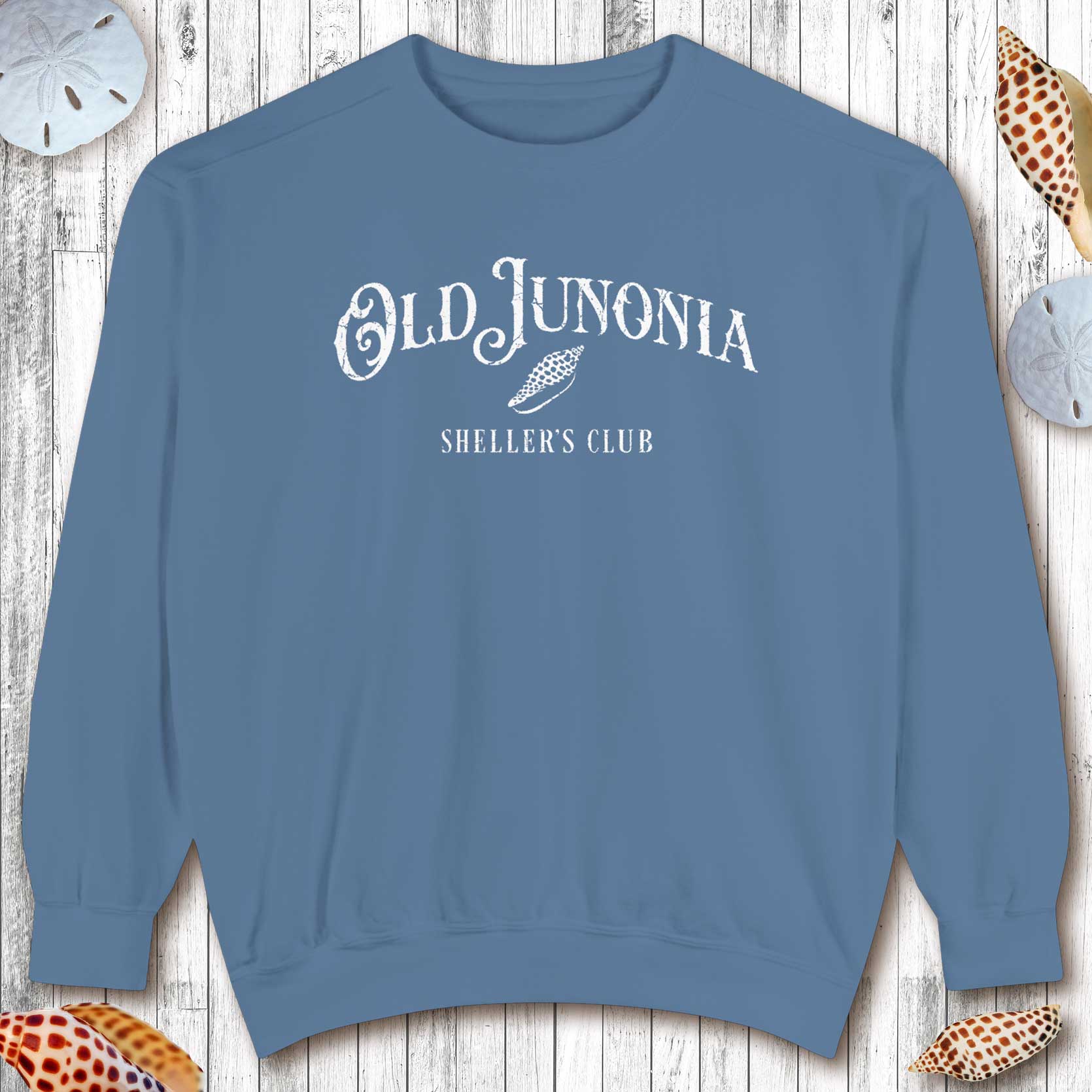 Blue sweatshirt with 'Old Junonia' text on a wooden surface with seashells.