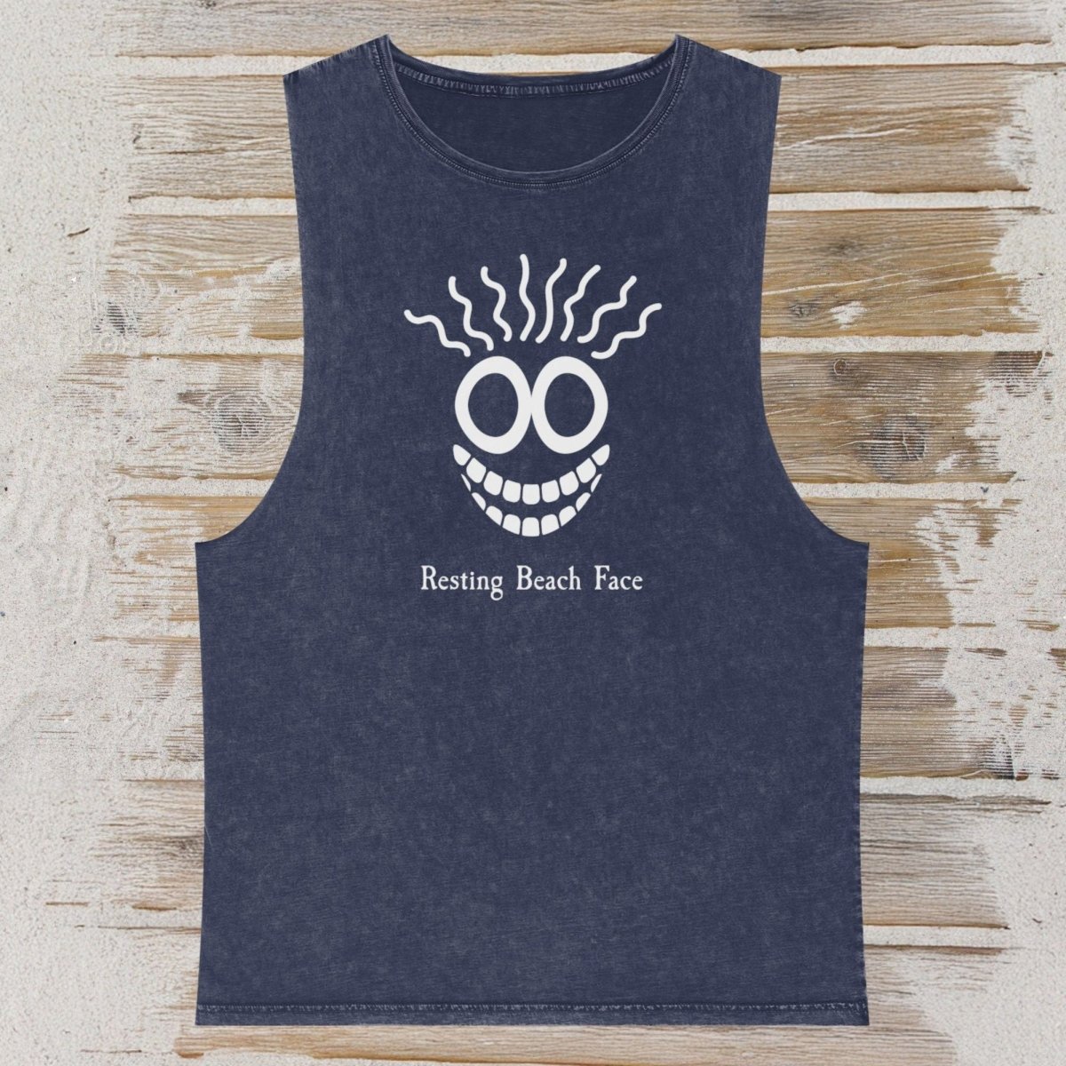 A sleeveless dark navy tank top with a white graphic of a smiling face and the text 'Resting Beach Face' printed on the front, displayed flat on a light wood plank background.