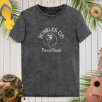 Black t-shirt with 'Bubbles Up! ParrotHeads' design on a wooden background with tropical elements.
