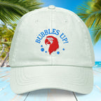 Pastel Mint cap with 'Bubbles Up!' design on a blue wooden surface with palm leaves in the background