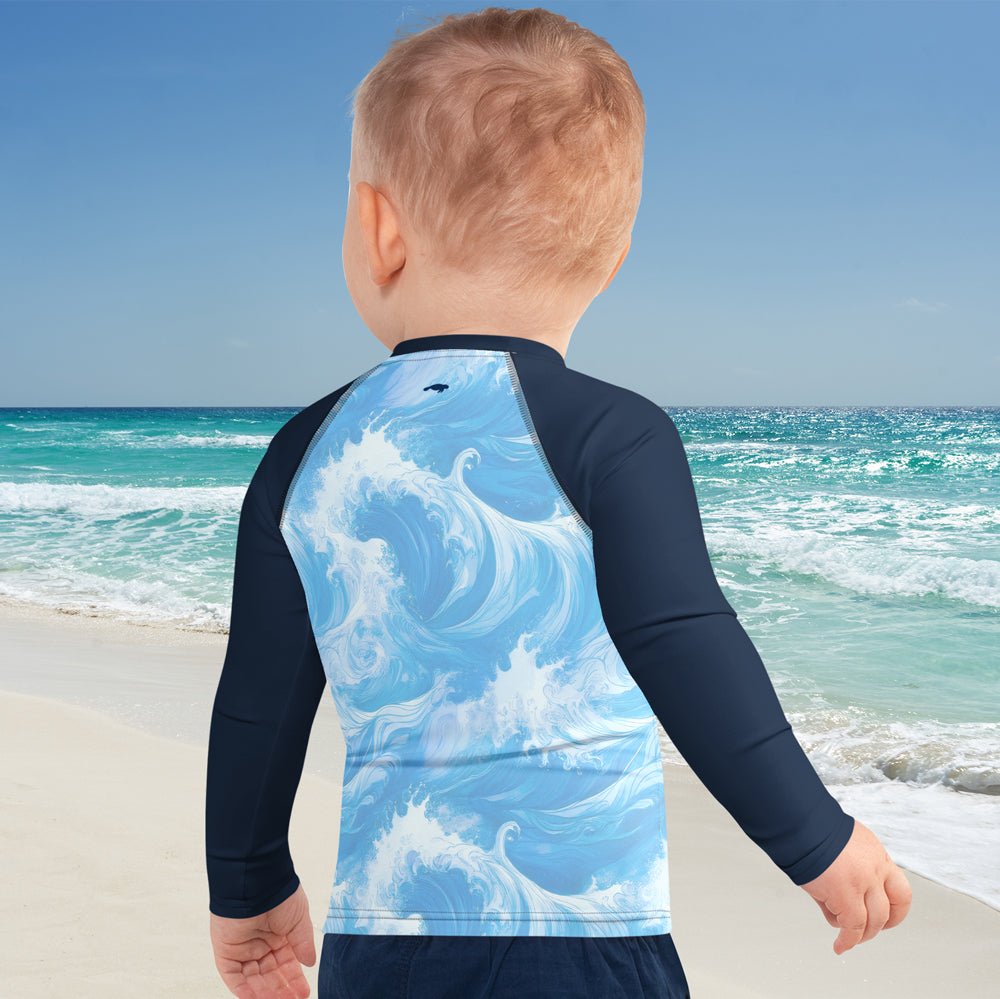 Child wearing a Clean Seas Society Rash Guard with ocean wave design and the CSS Manatee logo, standing on a beach